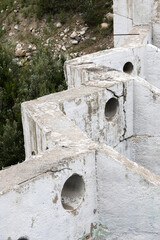 An abandoned concrete dam structure with circular openings and visible cracks in a natural setting