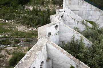 An old abandoned concrete dam with visible cracks and vegetation growing around it in nature