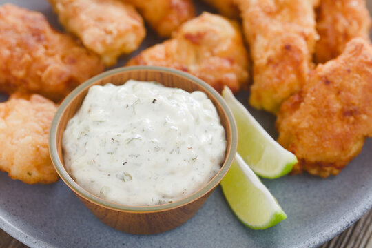 Fresh homemade tartar sauce made of mayonnaise, pickles, capers, herbs, salt and pepper, with fried fish pieces and lime wedges on the side (Selective Focus, Focus on the front of the sauce)