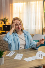 Young woman checks statement at home, eyes widening with alarm over unexpected expense. Girl sits...