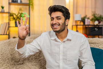 Indian young man at home confidently smiling and showing an OK hand gesture, expressing approval....