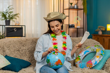 Woman tourist with inflatable swim ring at home thoughtfully examining world map globe planning...
