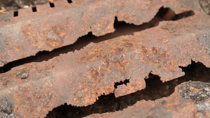 Detailed image showcasing a close-up view of a metal grate, heavily affected by rust and corrosion....
