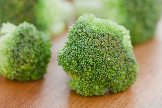 Fresh raw broccoli florets on wooden board (Very Shallow Depth of Field, Focus on the front of the first broccoli piece)