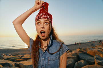 Young woman in modern boho-western denim street style holds red bandana over head with playful...