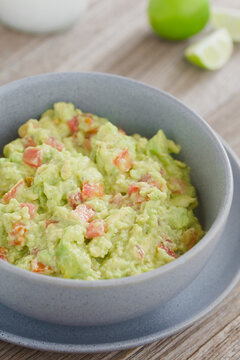 Freshly prepared homemade guacamole dip or salsa, made of avocado, tomato, lime juice, salt and pepper, served in blue bowl with lime wedges on the side (Selective Focus, Focus one third into the dip)