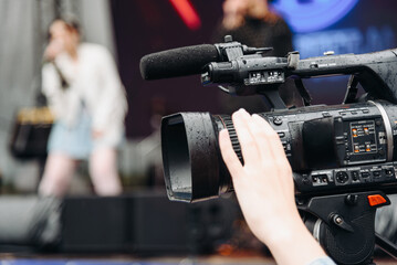 large black video camera on tripod, close-up view, videographer working at music festival in city park, rock group performing on stage