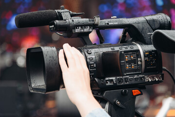 large black video camera on tripod, close-up view, videographer working at music festival in city park, rock group performing on stage