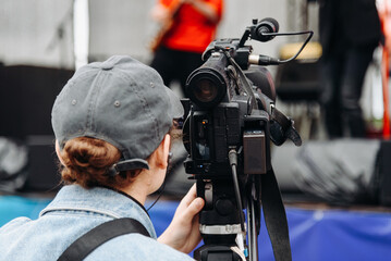 large black video camera on tripod, videographer working at music festival in city park, rock group performing on stage