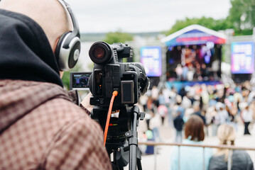 Obraz premium large black video camera on tripod outdoors, operator videographer shooting music festival and crowd of people outdoors, television work