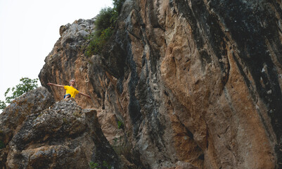 Adventurer in Yellow Top Standing on Rocky Terrain with Cliff Backdrop