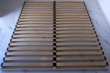 Fototapeta premium Wooden bed slats double frame on white marble floor, orthopedic mattress base, flexible plywood laths with black holders, minimal top view