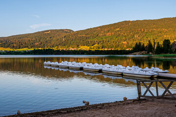 Tranquil Beach and Pedal Boats on lake at Sunset. Jura Mountains, France.