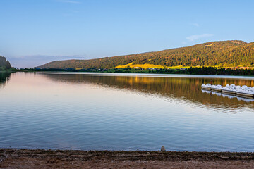 Tranquil Beach and Pedal Boats on lake at Sunset. Jura Mountains, France.