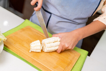 Chef cutting white corn on wooden board for peruvian ceviche