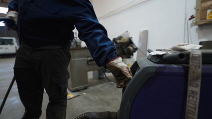 Welder wearing protective gloves operating a welding machine in a metalworking workshop