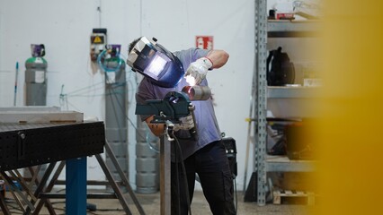 Welder joining metal pipes with welding torch, wearing protective gear in industrial workshop...