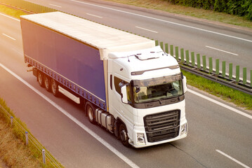 Modern White Cargo Transportation Truck with Blue Curtain Trailer Driving on Highway at Golden Hour