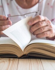 Close Up Of An Old Book With Woman Flipping Pages And Glasses On Light Wood Table