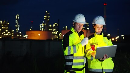 Petrochemical industry engineers teamwork using laptop computer at night on oil refinery construction site, technicians inspecting petroleum gas system, maintaining power and energy infrastructure.