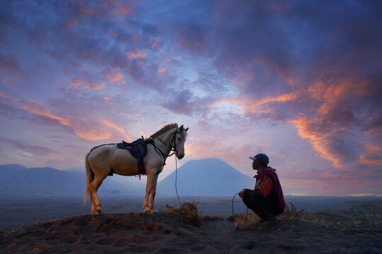 Man crouching next to his horse, Bromo Tengger Semeru National Park, East Java, Indonesia