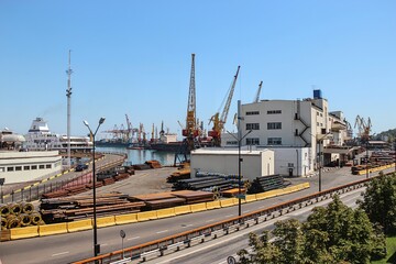 Industrial cargo port with cranes, pipes, and ships under clear sky
