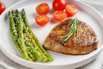 Close up, macro of tasty grilled beef steak served with green asparagus and cherry tomatoes on white plate, with cutlery. Perfect for food menu, diet, or culinary design concepts.