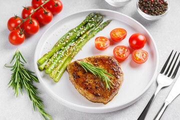 Close up, macro of tasty grilled beef steak served with green asparagus and cherry tomatoes on white plate, with cutlery. Perfect for food menu, diet, or culinary design concepts.