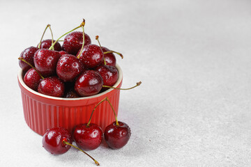 Red bowl filled with organic fresh sweet cherries with water drops on white stone surface with copy...