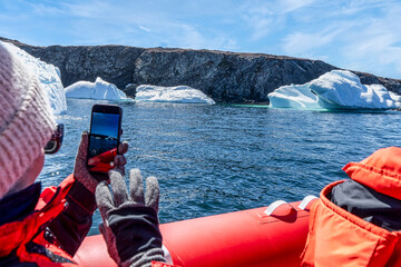 Rear view of a woman in a tourboat photographing Icebergs floating near the coastline, Newfoundland, Newfoundland and Labrador, Canada