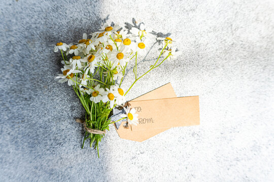 Overhead view of a Bunch of wild daisies with a blank gift tag lying on a table in sunlight