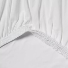White fitted bed sheet close-up showing elastic hem and smooth fabric texture for comfortable bedding solutions.