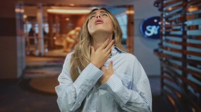 Blonde woman clutching throat and looking upward in striped shirt at airport terminal; choking distress.