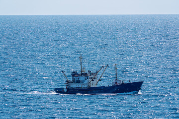 Fishing boat in blue sea and clear sky with birds flying overhead.