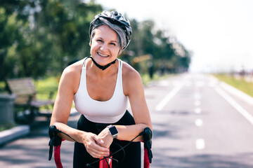 Smiling senior woman on red bicycle in helmet enjoying summer ride on empty park bike lane