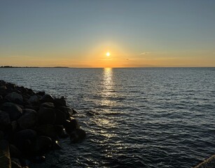 Sunset over calm Baltic sea, in Fehmarn, Germany. Sun shining from behind clouds and bright...