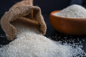 White sugar spilling from a burlap sack beside a full bowl