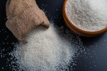 White sugar spilling from a burlap sack beside a full bowl