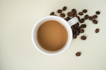 Flat lay of a white cup of coffee with coffee beans on a light background