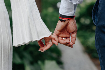close-up view of couple holding hands, young beautiful caucasian man and woman take each other hands, walking on pathway in park in summer, love and family concept, selective focus