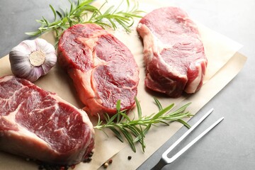 Pieces of raw beef meat, spices and carving fork on grey table, above view