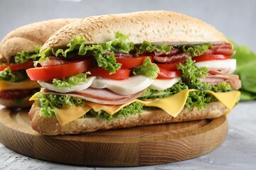 Tasty baguette sandwiches with ham, cheese and vegetables on grey textured table, closeup