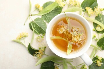 Fresh linden tea in cup and flowers on white table, flat lay