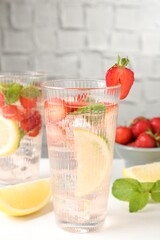 Tasty refreshing drink with strawberries, lemon and mint on white table, closeup