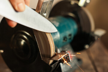 Man sharpening knife with bench grinder indoors, closeup
