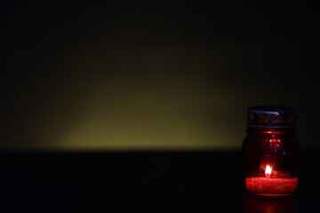 Grave lantern with burning candle on black table against green background. Space for text