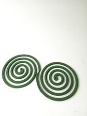 Two green mosquito coils arranged in a spiral shape on a white surface create an abstract design.