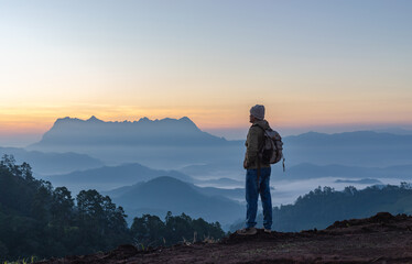 Male Hiker with backpack relaxing on top of rock mountain and enjoying sunset sky.
