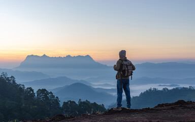 Male Hiker with backpack relaxing on top of rock mountain and enjoying sunset sky.