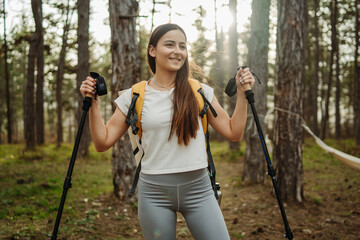 Young caucasian woman hiking or trekking through scenic forest with hiking poles	